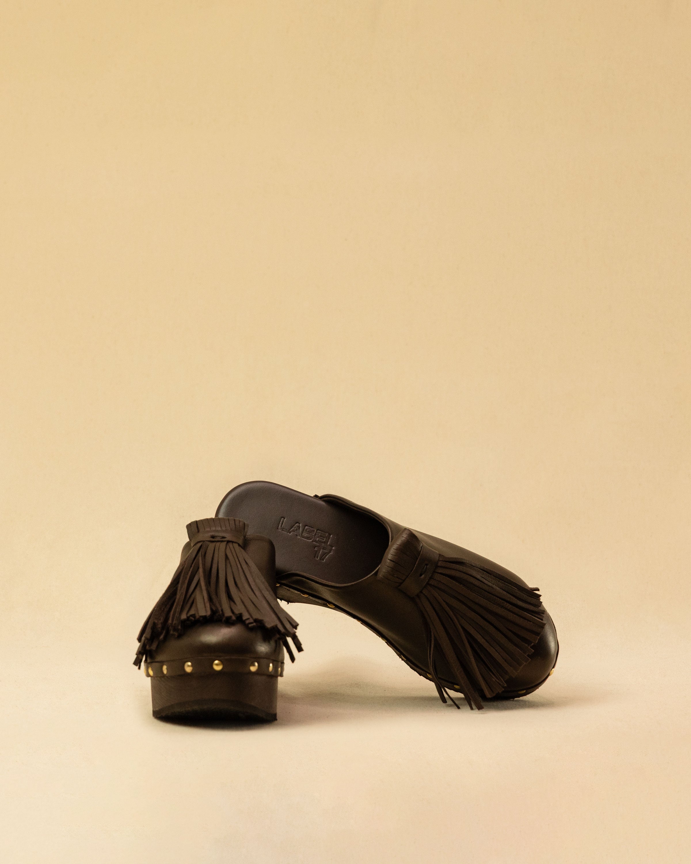 Clogs Choucha in dark brown by LABEL17, crafted from supple, vegetable-tanned lamb nappa leather. A large, soft pompom on top swings elegantly from left to right with each step, adding a playful yet refined touch. The shoe features a durable Vibram sole for comfort and stability. The artisanal craftsmanship enhances the overall aesthetic, making these clogs a true statement piece. Quiet luxury at its best. Handmade in Greece.