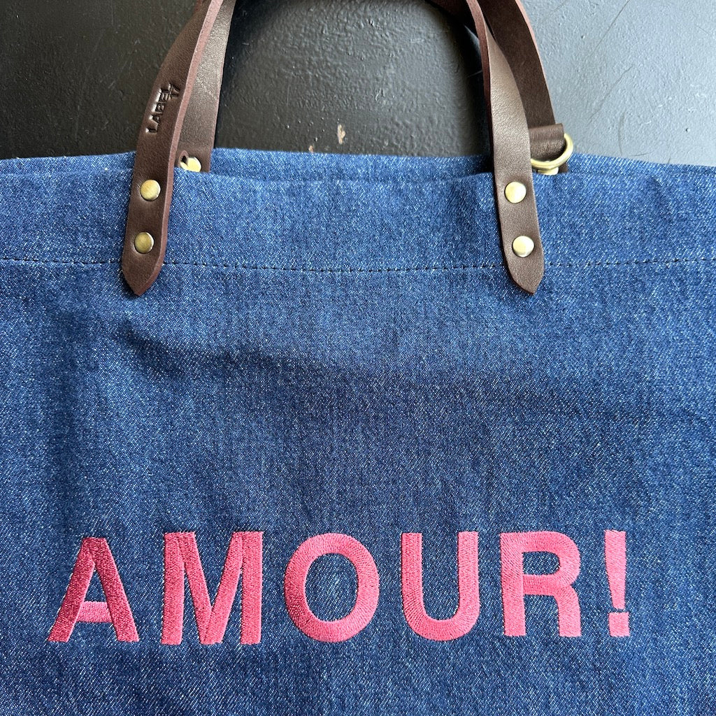 Bestickte Stofftasche von LABEL17 mit braunen Lederhenkeln und AMOUR Botschaft auf der Vorderseite. Hergestellt in Marokko